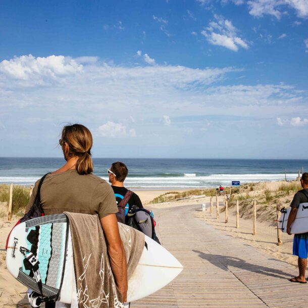 Trois amis marchent ensemble, planches de surf sous le bras, regardant l'océan, prêts à profiter d'une session de surf à l'océan.