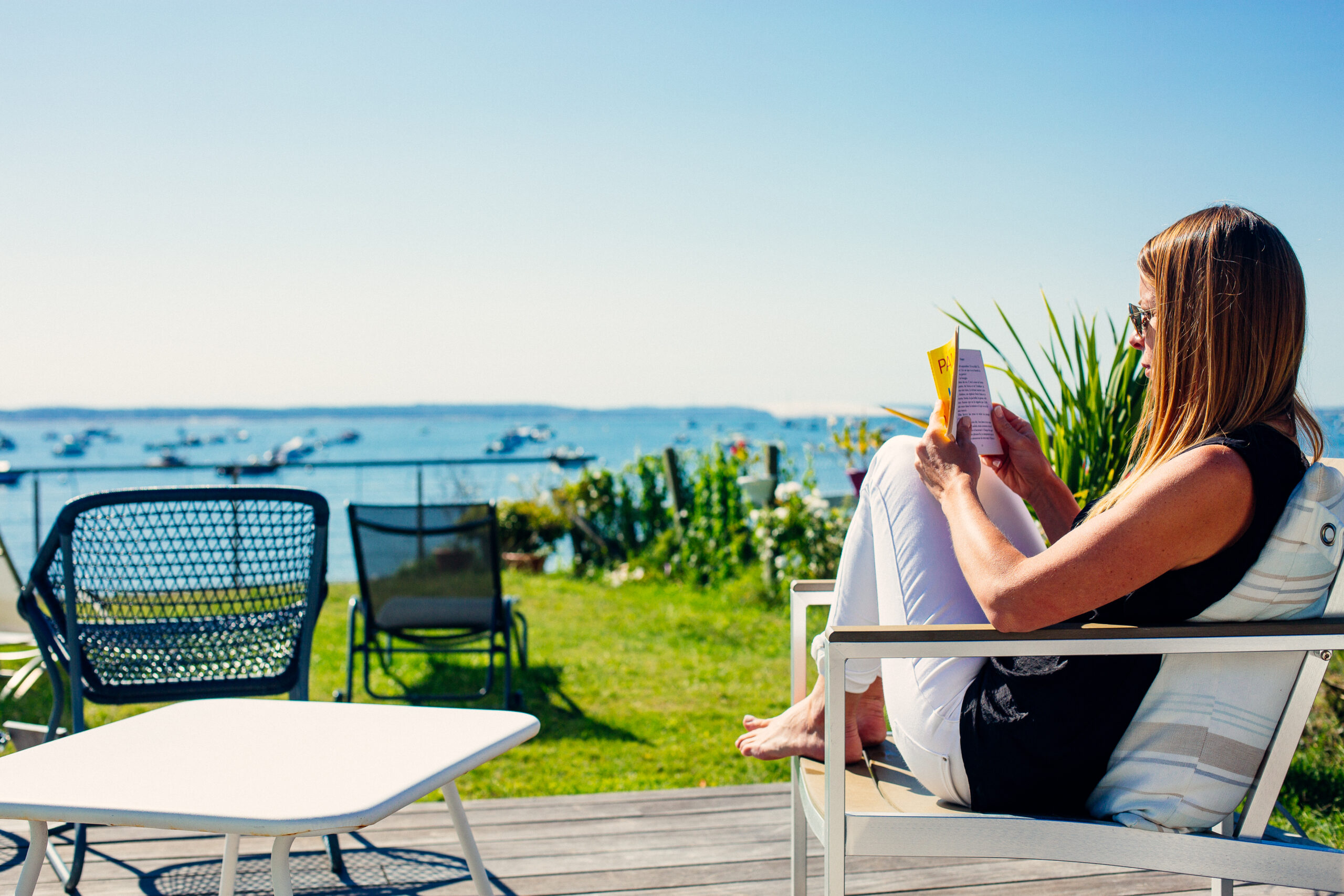 Une personne lit son livre sur sa terrasse avec la vue du bassin qu'on peut apercevoir. 
