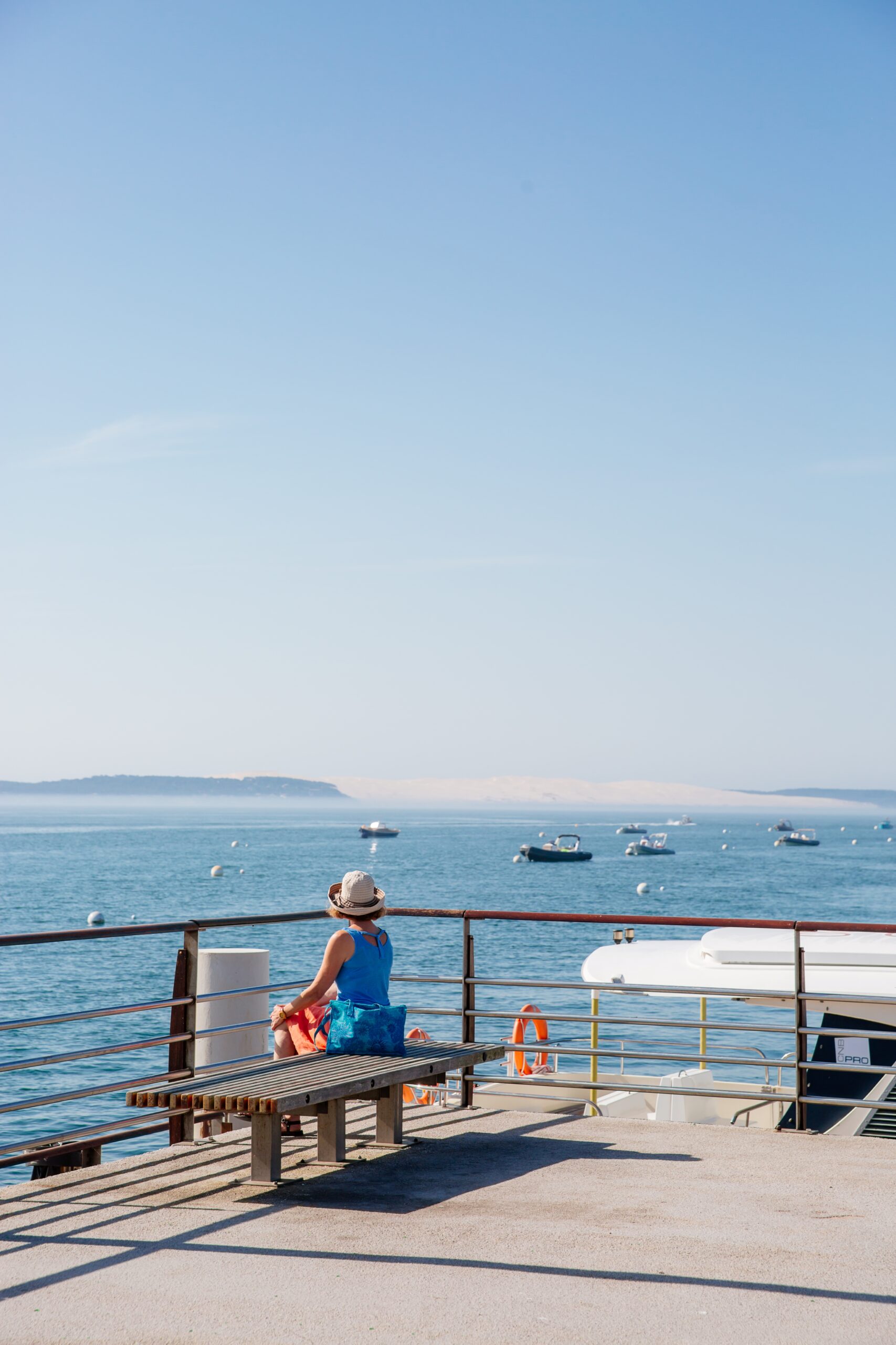 une femme est assise regard le bassin possé sur le port. 