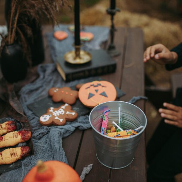 Table de fête Halloween décorée avec des biscuits en forme de citrouille, de squelette et de doigts ensanglantés, un seau en métal rempli de bonbons, et des chandeliers noirs, créant une ambiance festive et effrayante pour Halloween.