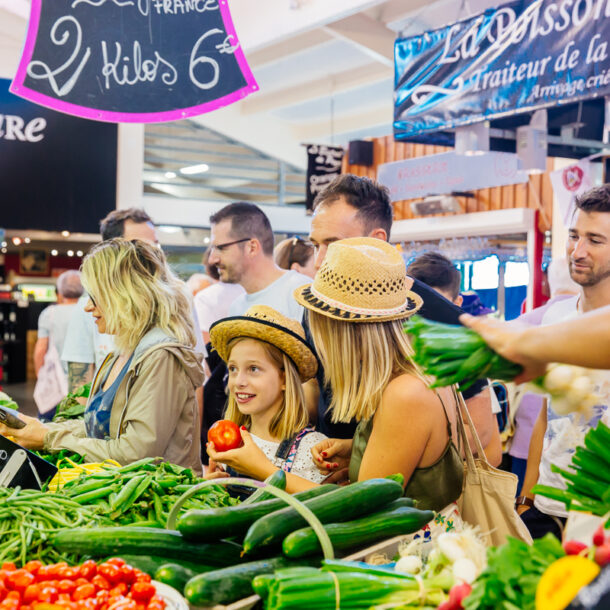 Une famille choisit des fruits et légumes frais sur un stand de producteurs locaux dans le marché couvert de Piraillan à Lège-Cap Ferret, sur le Bassin d’Arcachon.
